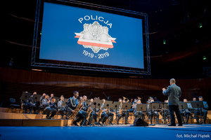 Orkiestra Komendy Wojewódzkiej Policji w Katowicach, w tle telebim z napisem: Policja 1919 - 2019.