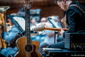 w centralnej części zdjęcia gitara na stojaku, w tle Orkiestra Komendy Wojewódzkiej Policji w Katowicach