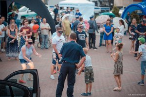 Festyn rodzinny. Policjant ruchu drogowego prowadzi prelekcje i pokaz dla uczestników festynu. Widoczny również radiowóz oznakowany