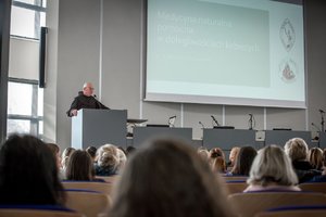 Zdjęcie kolorowe. Aula Komendy Wojewódzkiej Policji w Katowicach, do uczestniczek zwraca się jeden z prelegentów