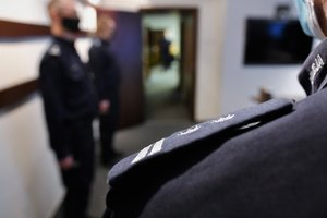 Na pierwszym planie ramię policjanta pagonem młodszego inspektora, w tle policjanci oczekujący na generała.