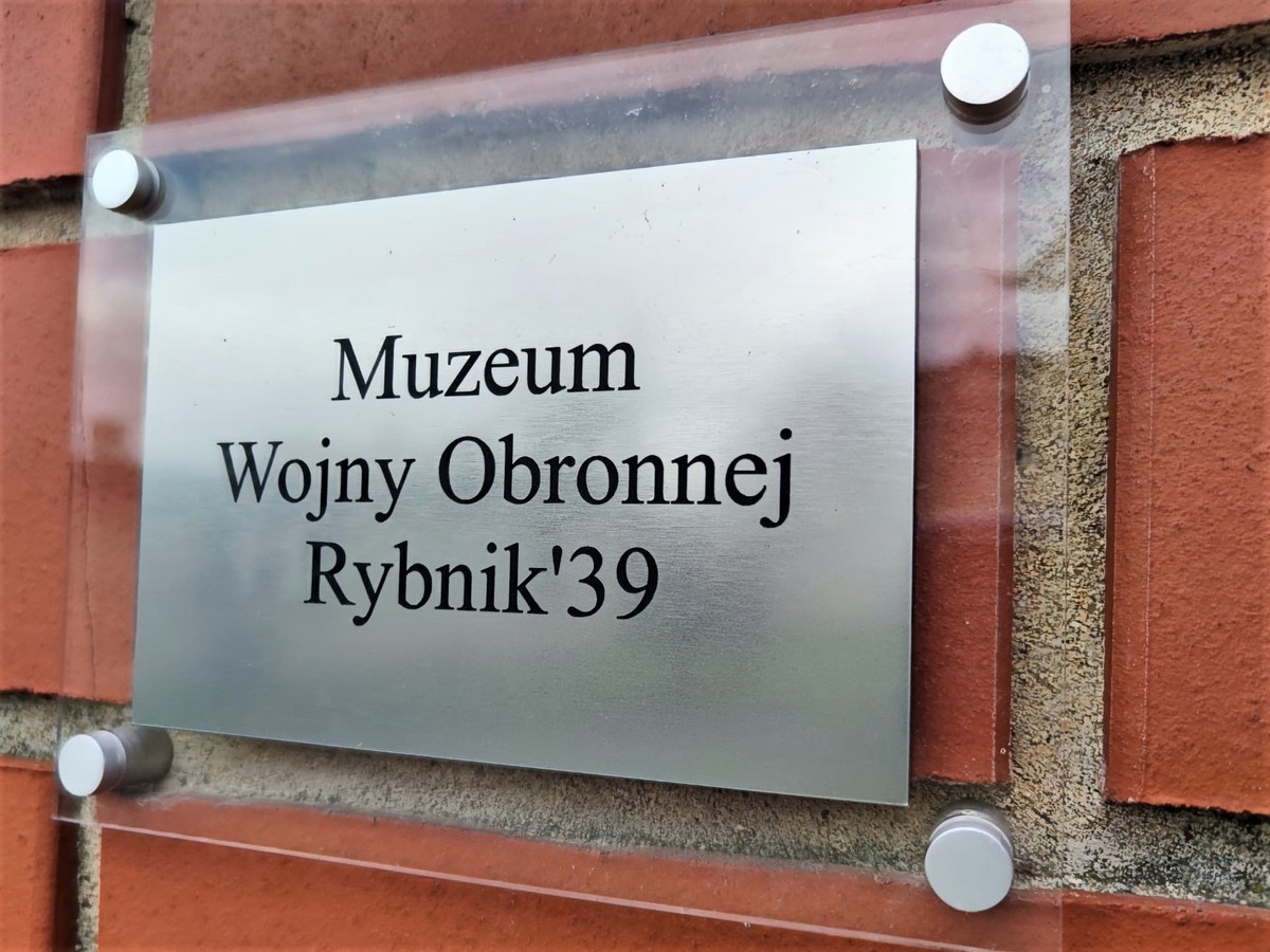 Zdjęcie kolorowe przedstawia tabliczkę informacyjną o treści: Muzeum Wojny Obronnej Rybnik`39.