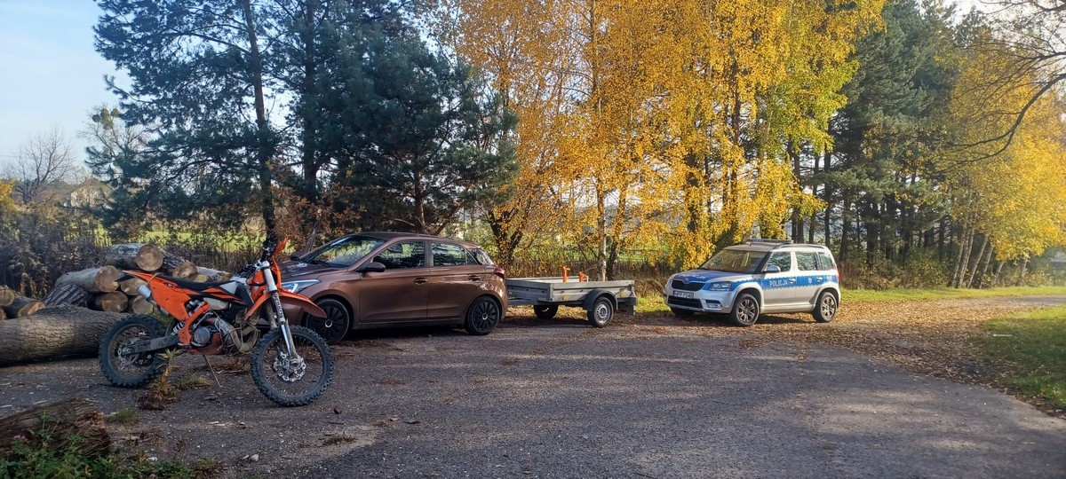 Zdjęcie kolorowe przedstawia samochód z przyczepką, a obok stoi motocykl typu cross, a za nimi radiowóz policyjny.