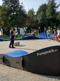 fotografia przedstawia policjanta na terenie pumptracka, który prowadzi rozmowę z dziećmi