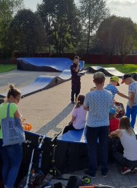 fotografia przedstawia policjanta, który omawia z dziećmi zasady bezpieczeństwa. Wszyscy znajdują się na terenie Pumptracka w Pawłowicach