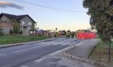 fotografia przedstawia policjantów i strażaków prowadzących czynności na miejscu wypadku drogowego. W oddali widać LPR, z prawej strony widoczny jest czerwony parawan.