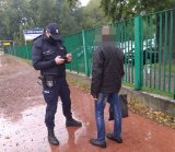 Na fotografii widać stojącego policjanta, przed nim stoi mężczyzna w czarnej kurtce. Oboje znajdują się chodniku. Pada deszcz