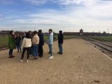 Fotografia przedstawia grupę młodzieży na tle bramy Obozu Koncentracyjnego w Birkenau