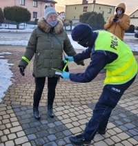 Pora dzienna. Umundurowany policjant zakłada na ręke kobiety opaskę odblaskową