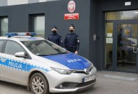 Na zdjęciu widoczni dwaj policjanci stojący obok radiowozu przed budynkiem Komisariatu Policji w Miedźnej. Pora dzienna.