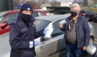 Na zdjęciu mężczyzna bierze maseczkę z pudełka, które trzyma policjant. Pora dzienna.