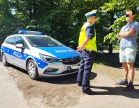 Zdjęcie kolorowe: mężczyzna z policjantem, w tle radiowóż