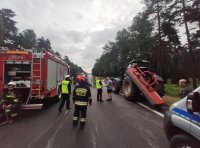 Zdjęcie kolorowe wóz straży pożarnej, widoczny ciągnik rolniczy, policjanci i strażacy na miejscu zdarzenia