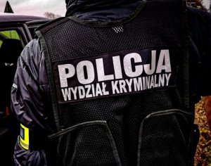 Zdjęcie kolorowe: policjant stoi tyłem, widoczny napis na jego plecach Policja, Wydział Kryminalny