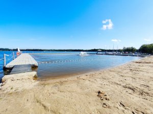 Zdjęcie kolorowe: plaża, pomost, w tle łódki