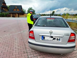 Zdjęcie kolorowe: policjant stoi obok samochodu, przeprowadza kontrolę