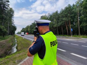 Zdjęcie kolorowe: policjant ruchu drogowego mierzy prędkość przejeżdżających pojazdów