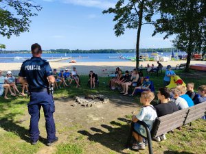 Zdjęcie kolorowe: policjant stoi na środku, dzieci siedzą dookoła