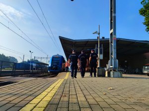 Zdjęcie kolorowe: dwóch funkcjonariuszy Ochrony Kolei i jeden policjant patrolują teren wzdłuż peronu