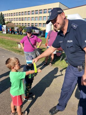 Zdjęcie kolorowe: policjant zakłada dziecku odblask na rękę