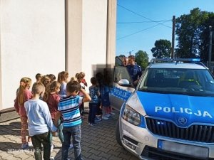 Zdjęcie kolorowe: dzieci stoją przed radiowozem, obok stoją policjanci