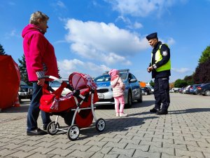 Zdjęcie kolorowe: policjant, dziewczynka i starsza Pani na tle radiowozu