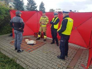 Zdjęcie kolorowe: policjanci ruchu drogowe, mężczyzna i strażak podczas szkolenia z pierwszej pomocy