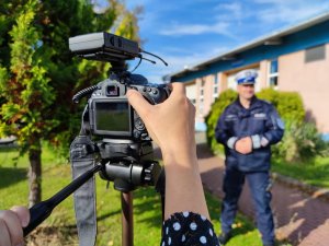 Zdjęcie kolorowe: na pierwszym planie widoczny aparat, w tle widoczny policjant ruchu drogowego