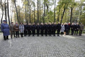 Zdjęcie kolorowe: na tle parku stoją mężczyźni i kobiety, umundurowani żołnierze i policjant.