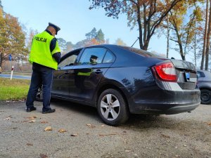 Zdjęcie kolorowe: umundurowany policjant stoi obok samochodu osobowego podczas kontroli drogowej.