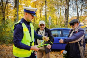 Zdjęcie kolorowe:Policjant ruchu drogowego podczas wręczania odblasków przechodniom