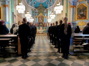 Zdjęcie kolorowe wnętrza kościoła, tyłem widoczni uczestnicy mszy.