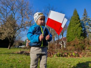 Zdjęcie kolorowe: mały chłopczyk trzyma w rękach dwie małe flagi