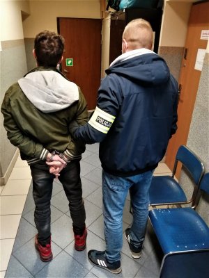 Zdjęcie kolorowe: policjant wraz z mężczyzną stoją tyłem w korytarzu