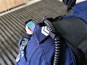 Zdjęcie kolorowe: umundurowany policjant dokonuje sprawdzenia na urządzeniu mobilnym