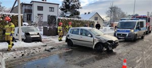 Zdjęcie kolorowe: uszkodzony pojazd w wyniku zdarzenia drogowego, w tle widoczni uczestnicy i policyjny radiowóz