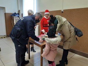 Zdjęcie kolorowe: umundurowany policjant rozdaje dzieciom odblaski