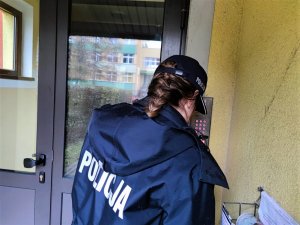 Zdjęcie kolorowe: umundurowana policjantka stoi przed domofonem w bloku