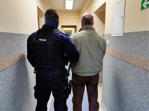 Zdjęcie kolorowe: umundurowany policjant z zatrzymanym w korytarzu