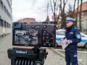 Zdjęcie kolorowe: widoczne aparat na statywie. Na wyświetlaczu umundurowany policjant ruchu drogowego.