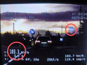 Zdjęcie kolorowe: widoczny samochód osobowy zarejestrowany przez wideorejestrator gdy jedzie z prędkością 103 km/h. Tuż przed nim zaznaczony znak przejścia dla pieszych