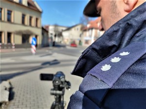 Zdjęcie kolorowe: widoczny umundurowany policjant ruchu drogowego, który nagrywa ruch kołowy odbywający w rejonie przejść dla pieszych