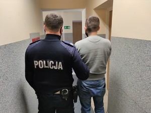 Zdjęcie kolorowe: umundurowany policjant z zatrzymanym mężczyzną w korytarzu