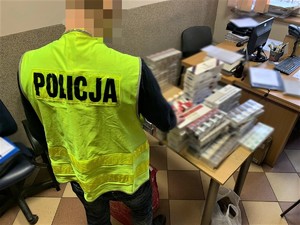 Zdjęcie kolorowe: policjant przy stole na którym leżą zatrzymane papierosy