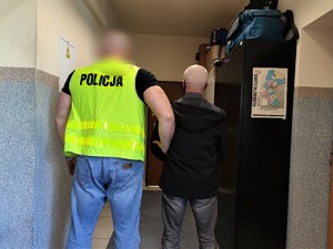 Zdjęcie kolorowe: policjant wraz z zatrzymanym mężczyzną w korytarzu