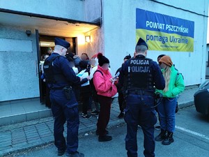 Zdjęcie kolorowe: dwóch umundurowanych policjantów przed budynkiem rozdaje ulotki informacyjne