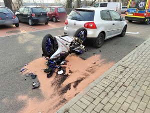 Zdjęcie kolorowe: wywrócony motocykl, a przed nim samochód osobowy