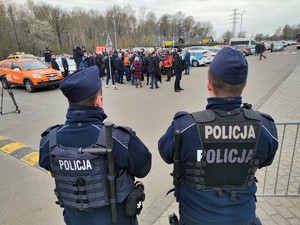 Zdjęcie kolorowe: dwóch umundurowanych policjantów. W tle widoczny tłum ludzi.