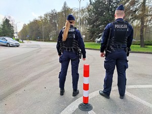 Zdjęcie kolorowe: na pierwszym planie dwóch umundurowanych policjantów stoi przy drodze, w tle radiowóz policyjny i policjant ruchu drogowego