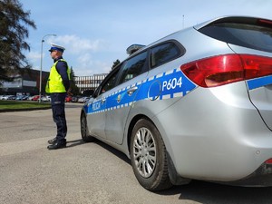 Zdjęcie kolorowe: umundurowany policjant ruchu drogowego przy oznakowanym radiowozie